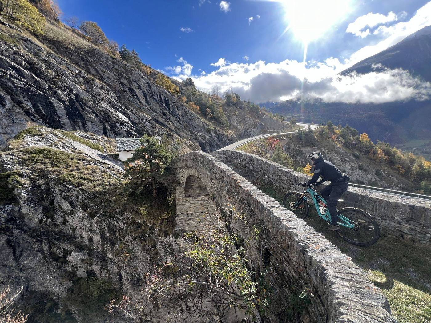 Rider überquert eine alte Steinbrücke auf einem Herbsttrail im Oberwallis