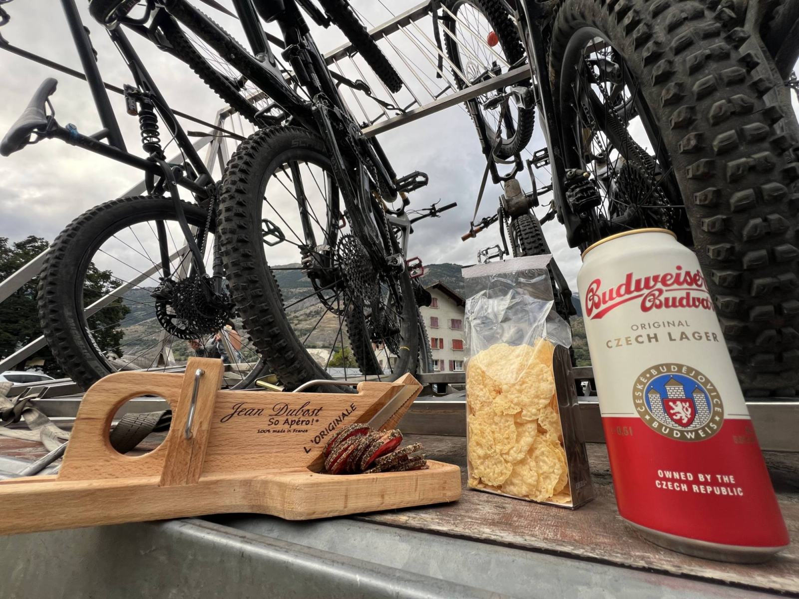 End-of-day apéro on the Exoride trailer, dried meat and a beer, bikes racked behind