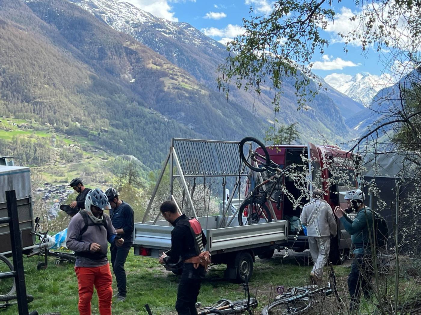 Group of mountain bikers gearing up at the drop-off, in front of the Exoride van and trailer, above a Valais valley