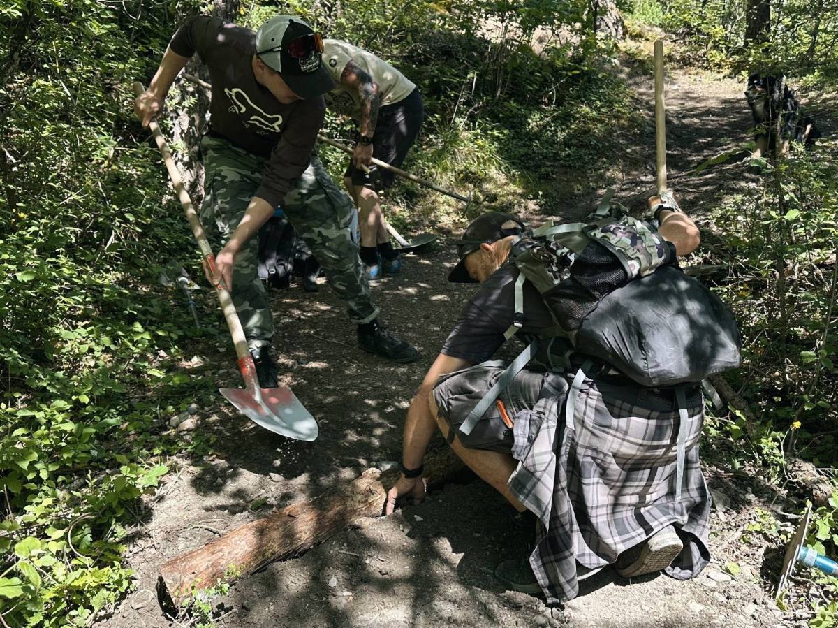 Volunteers repairing a mountain bike trail in a Valais forest, shovels in hand and a log set across the path to shed water