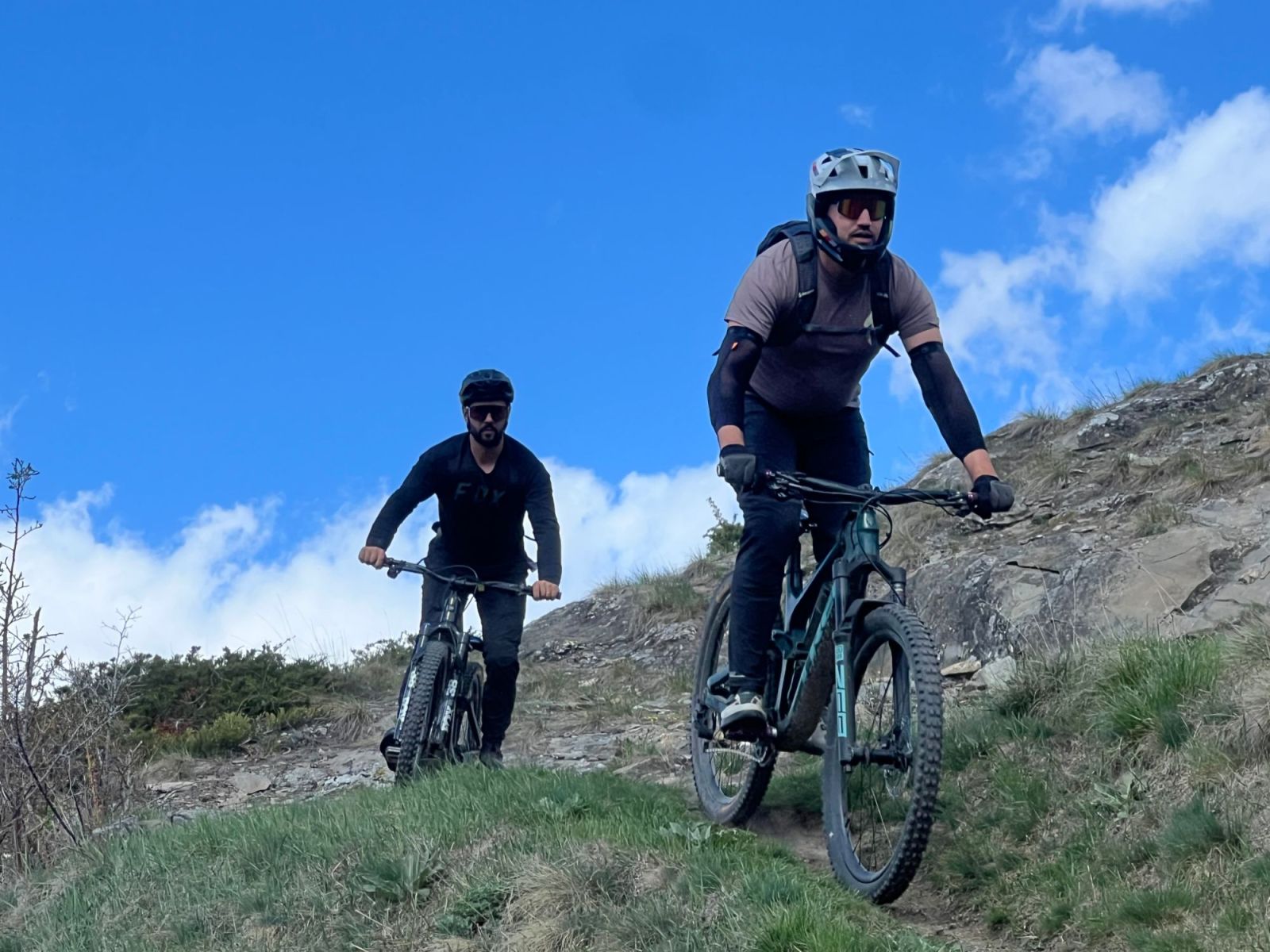 Two riders on enduro e-bikes riding together along a rocky ridge in Valais