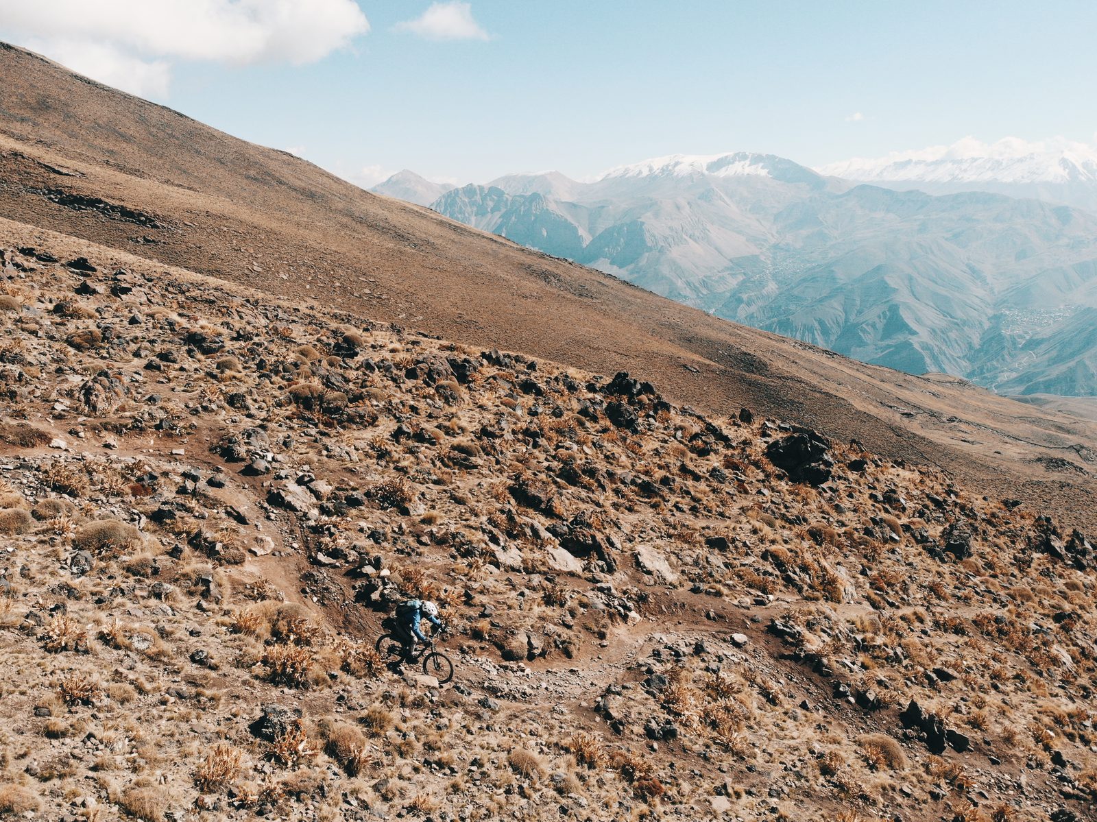 Un rider sur une pente d'altitude en Iran, sommets enneigés à l'horizon, préparer son séjour VTT avec Exoride