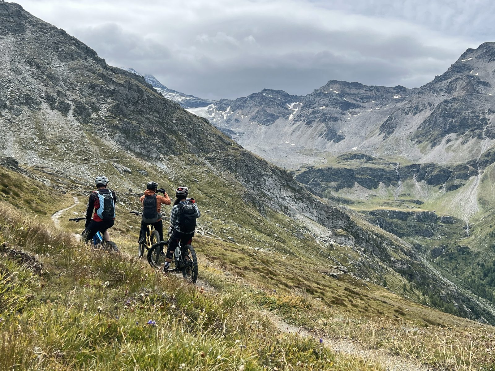 Trois riders regroupés au-dessus d'une vallée alpine du Valais, préparer son séjour VTT avec Exoride