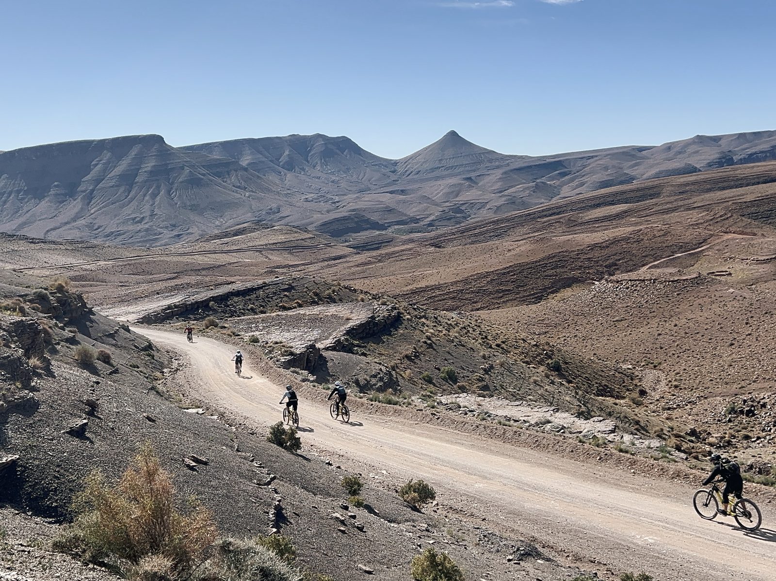 Biker auf einer breiten, flowigen Piste, die sich durch ein Tal im Süden Marokkos schlängelt, Reise Zagoride in Marokko mit Exoride