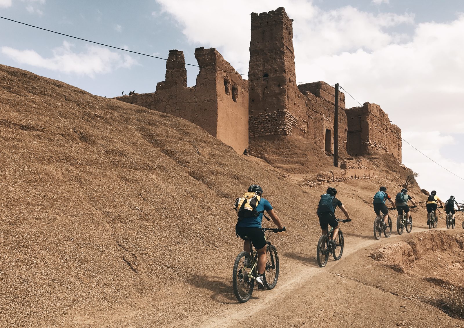 Eine Gruppe von Bikern fährt an einer Lehmkasbah vorbei, auf einer Piste im Süden Marokkos, Reise Zagoride in Marokko mit Exoride